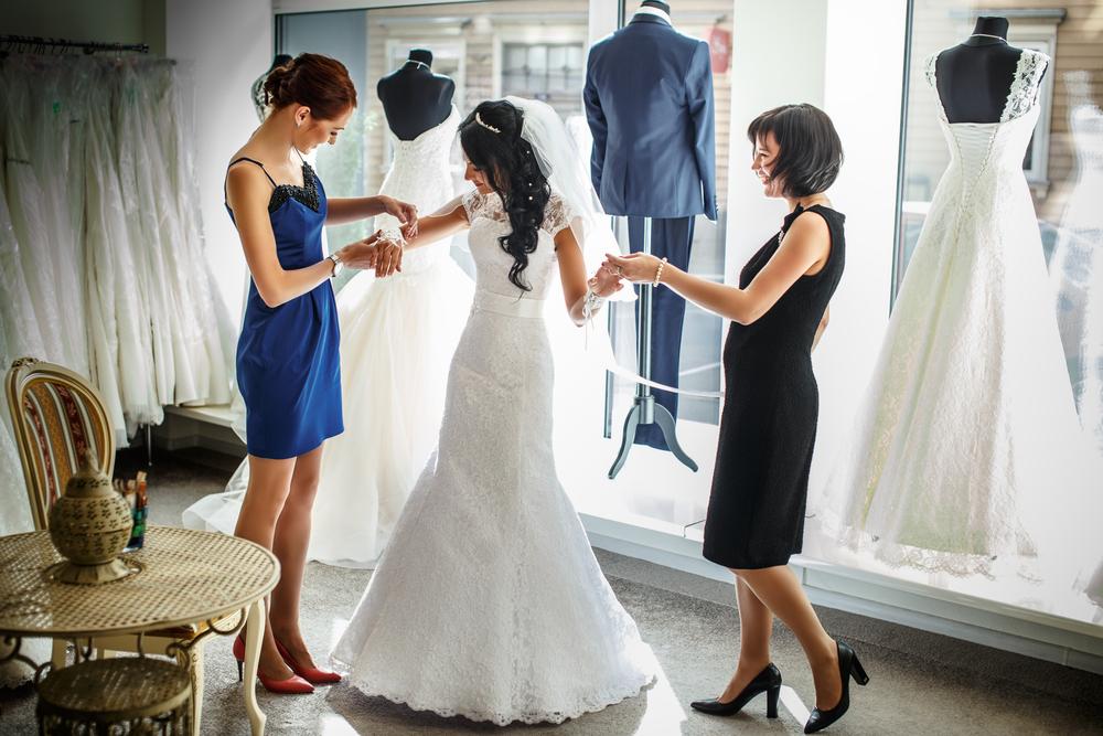 Female trying on wedding dress in a shop with two women assistants.