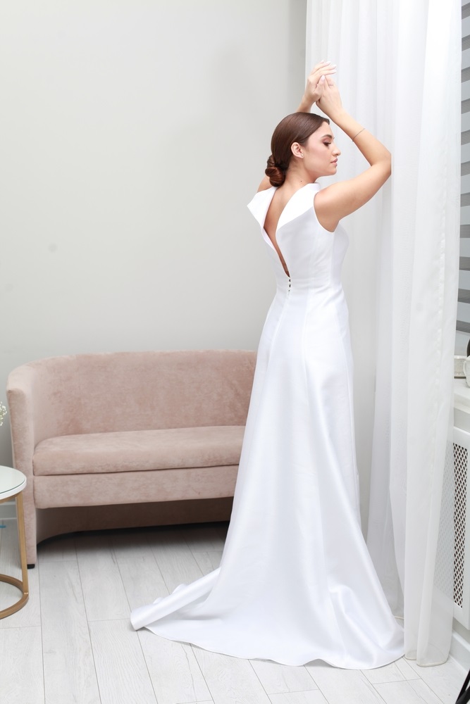 Alt text: Fashion studio photo of delicate brunette bride in simple minimalist luxurious dress. Wedding salon.